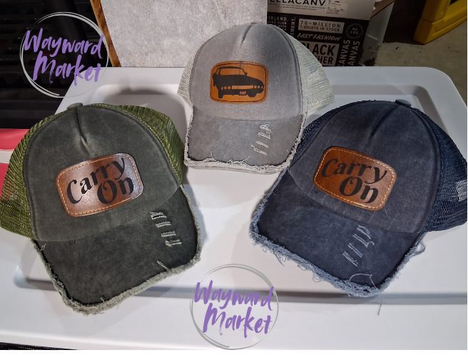 Three distressed hats with 'Carry On' patches on a tray, branded 'Wayward Market'.