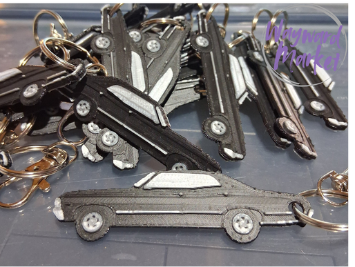 Collection of car-shaped keychains on a flat surface with 'Wayward Market' branding.